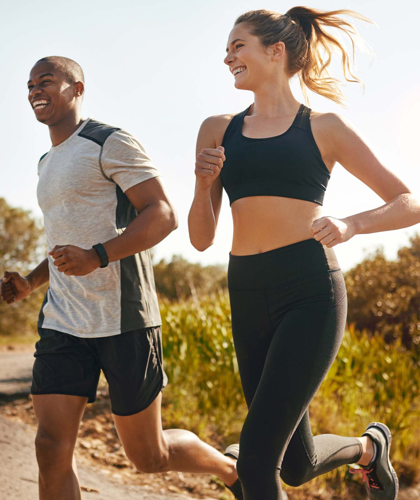 Pareja sonriente corriendo juntos por un sendero rodeado de naturaleza, ejemplificando un estilo de vida activo y saludable. Esta escena resalta la importancia de una protección solar efectiva como la que ofrece el protector solar deportivo &